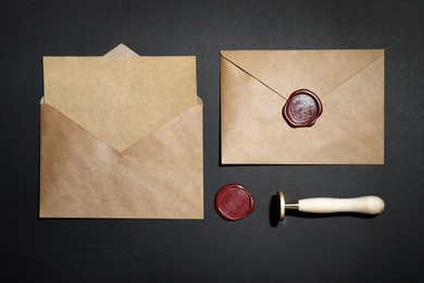 Envelopes with wax seal and stamp on black background, flat lay