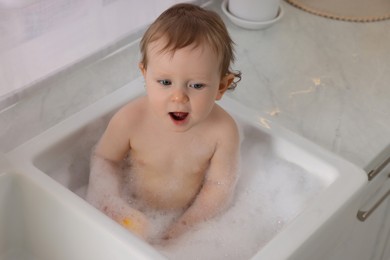 Photo of Cute little baby bathing in sink indoors
