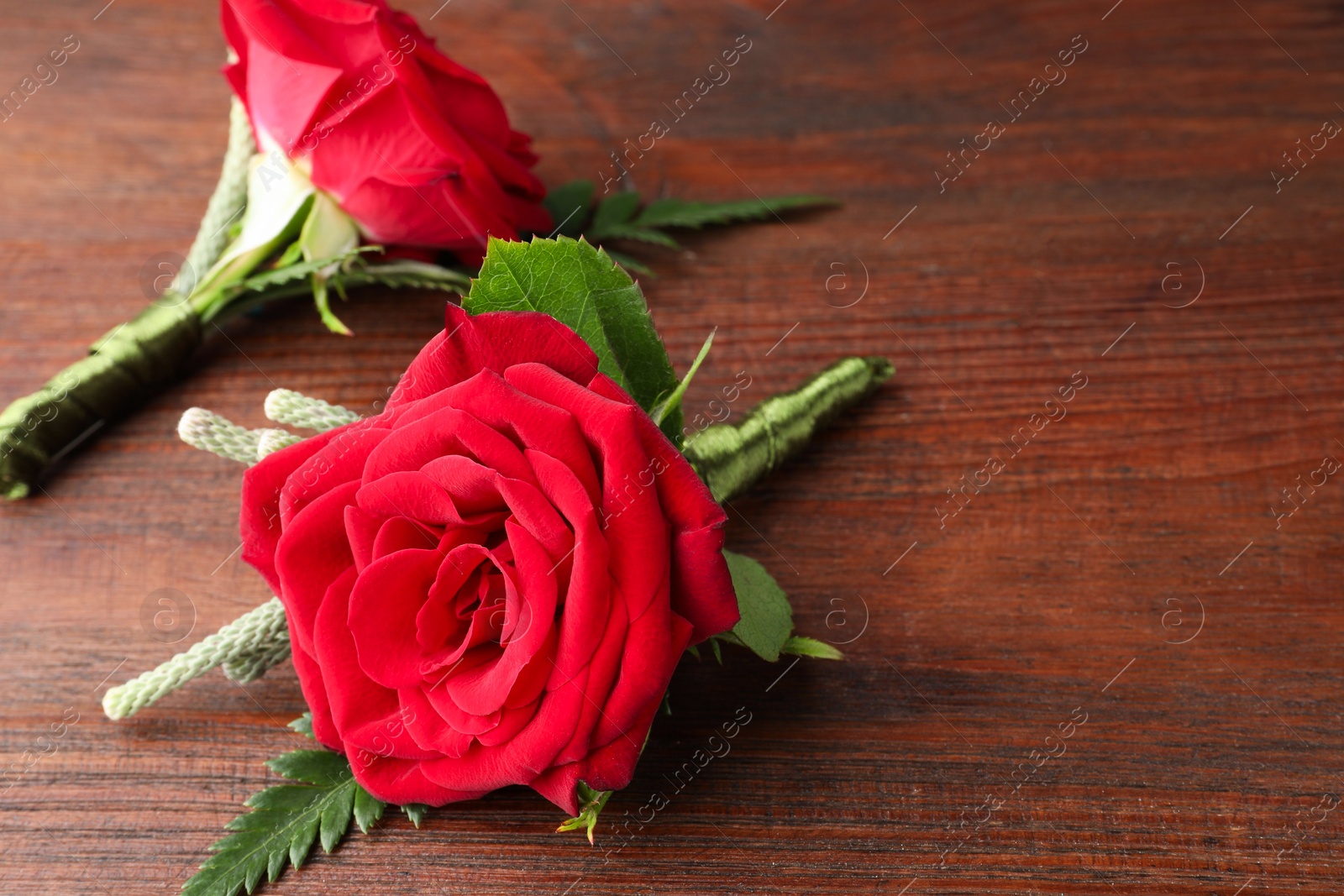 Photo of Two stylish red boutonnieres on wooden table, space for text