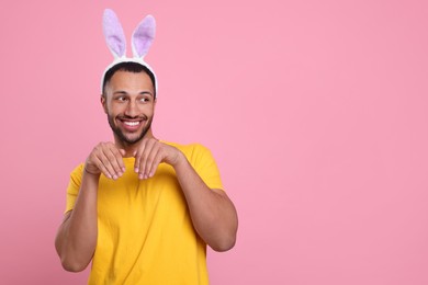 Happy African American man in bunny ears headband on pink background, space for text