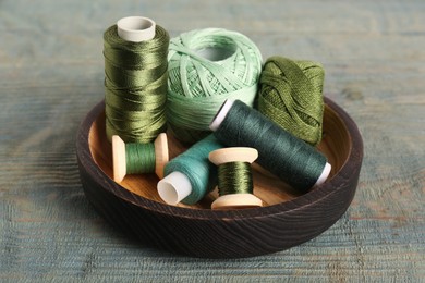 Photo of Color sewing threads in bowl on light blue wooden table