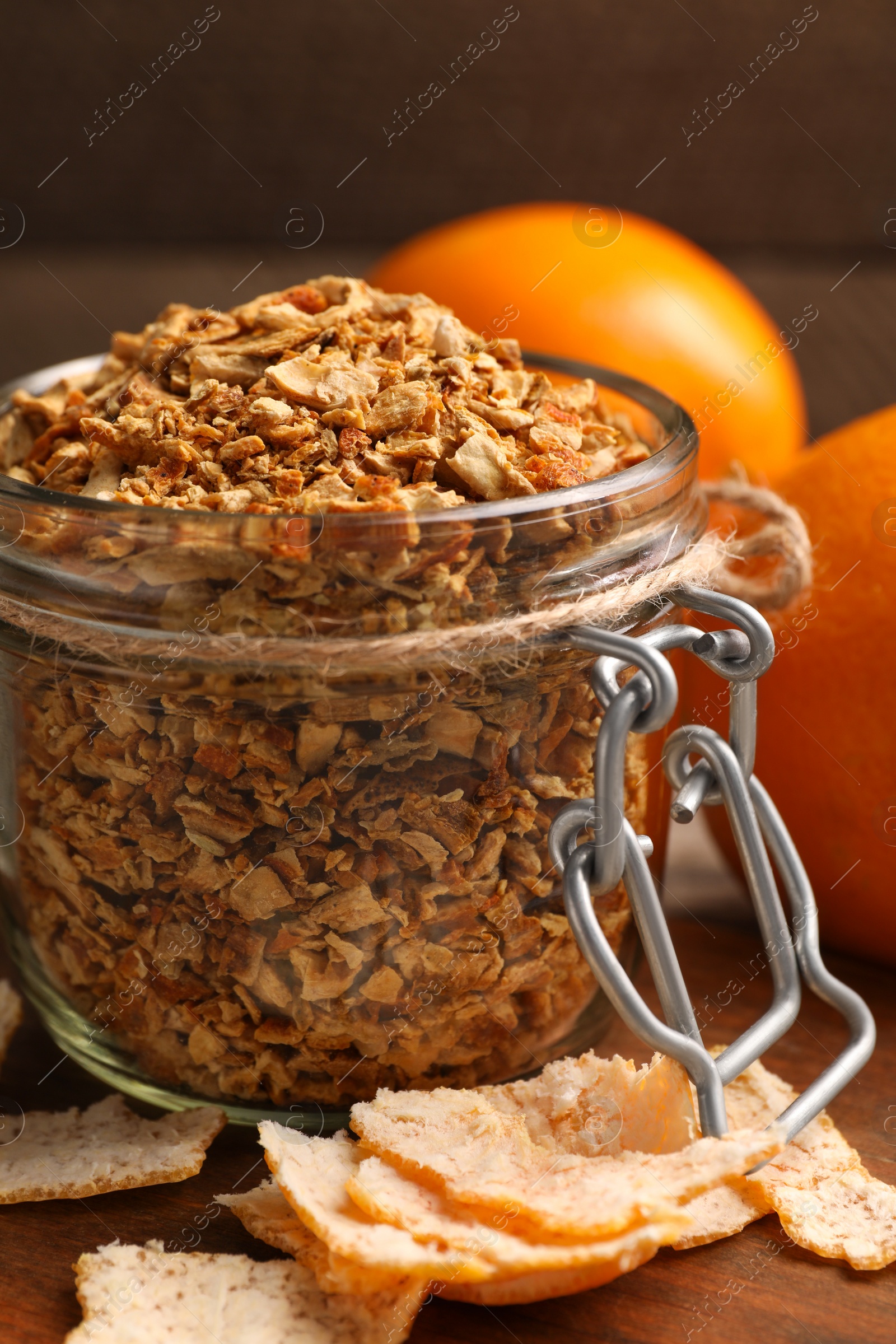 Photo of Jar of dried orange zest seasoning and fresh fruits on wooden table, closeup