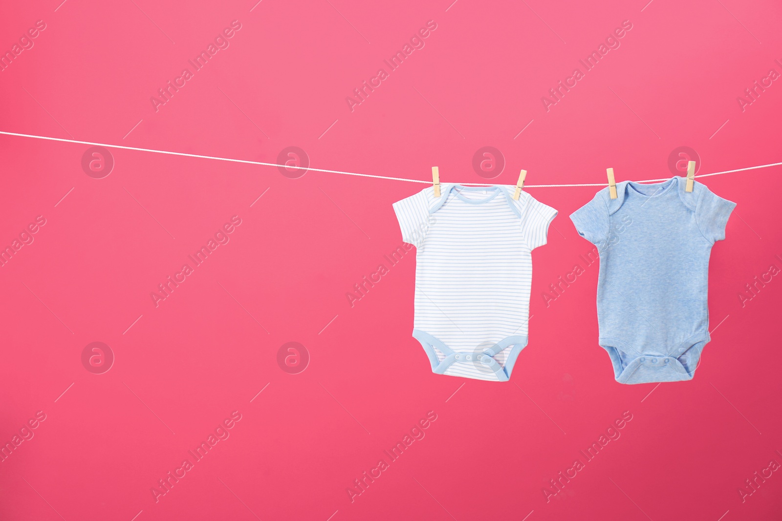 Photo of Baby onesies hanging on clothes line against pink background, space for text