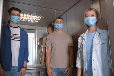 Photo of Group of people with face masks in elevator. Protective measure