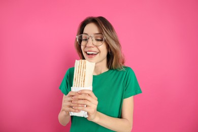 Photo of Emotional young woman with delicious shawarma on pink background