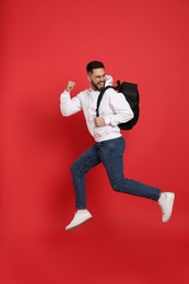 Emotional man with stylish backpack jumping on red background