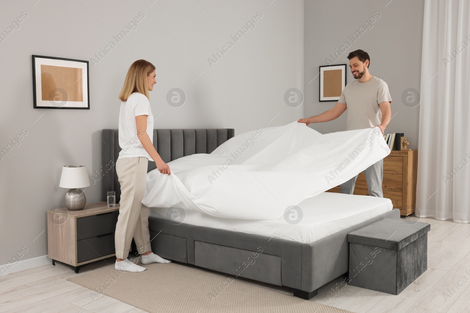 Photo of Couple changing bed linens in room. Domestic chores