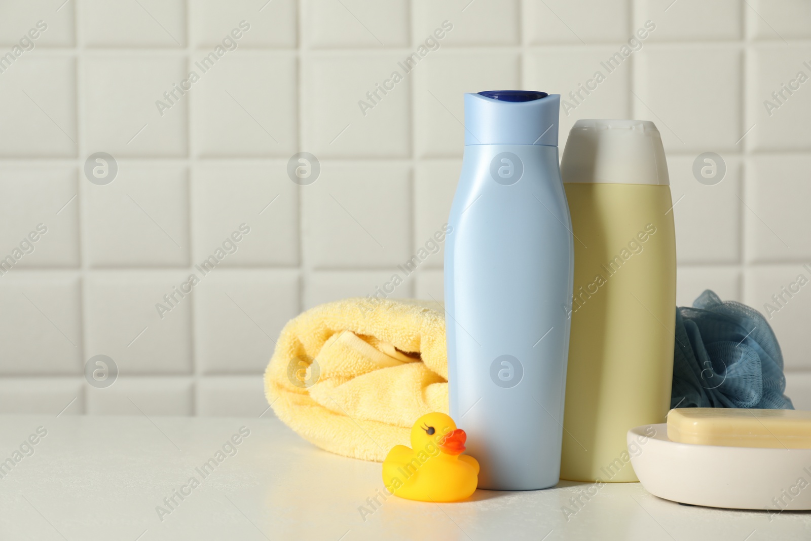Photo of Baby cosmetic products, bath duck, sponge and towel on white table against tiled wall. Space for text