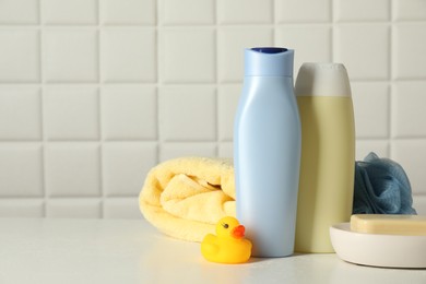 Baby cosmetic products, bath duck, sponge and towel on white table against tiled wall. Space for text