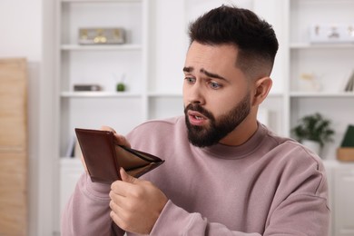 Photo of Confused man with empty wallet at home