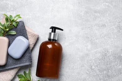 Photo of Soap bars, liquid dispenser and terry towels on light grey table, flat lay. Space for text