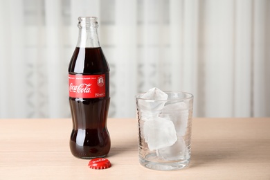 Photo of MYKOLAIV, UKRAINE - NOVEMBER 15, 2018: Bottle of Coca Cola and glass with ice cubes on table indoors