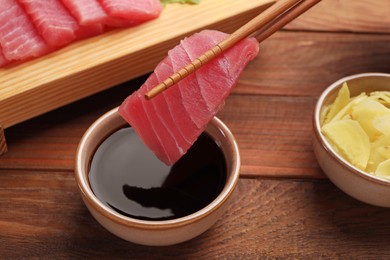 Photo of Dipping tasty sashimi (piece of fresh raw tuna) into soy sauce at wooden table