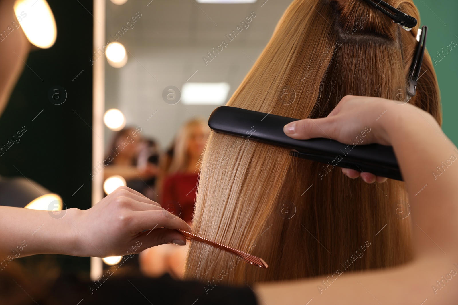 Photo of Stylist straightening woman's hair with flat iron in salon