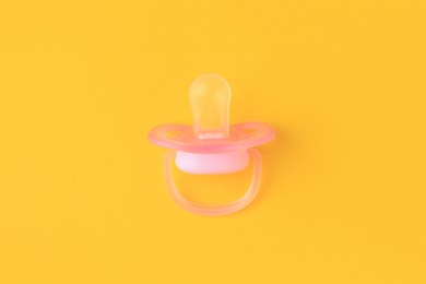 One new baby pacifier on orange background, top view