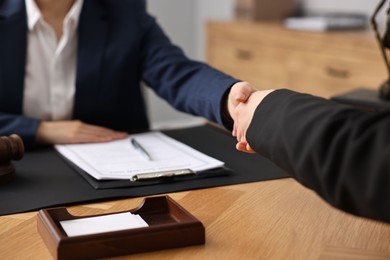 Notary shaking hands with client at wooden table in office, closeup