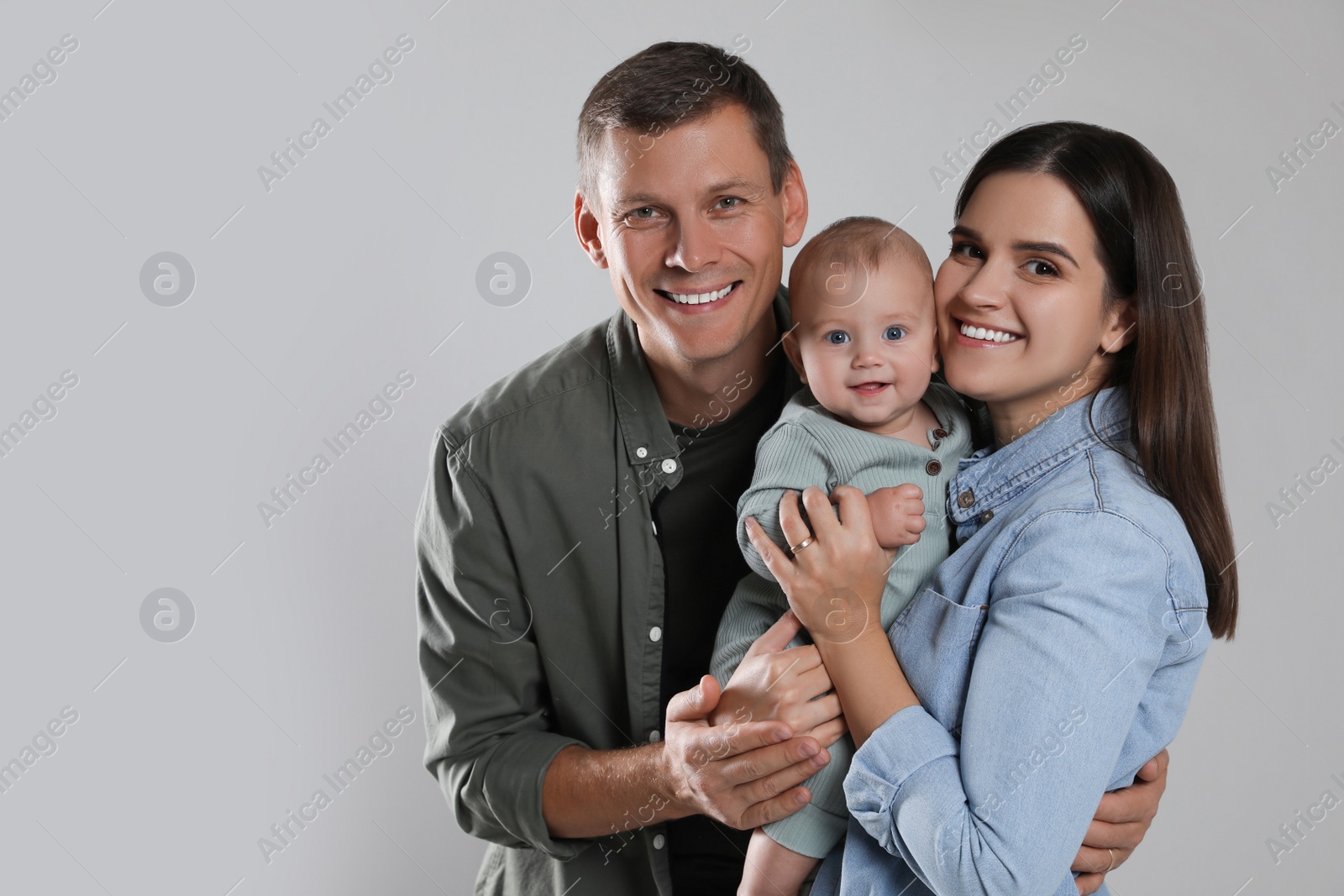 Photo of Happy family. Couple with their cute baby on grey background