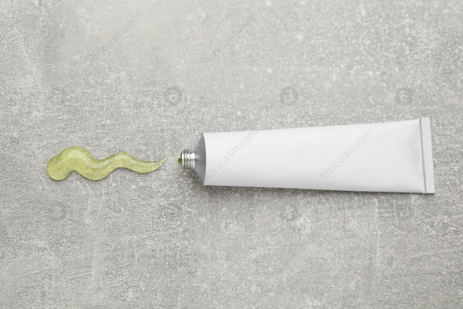 Photo of Open white tube with ointment on light grey table, top view. Space for text