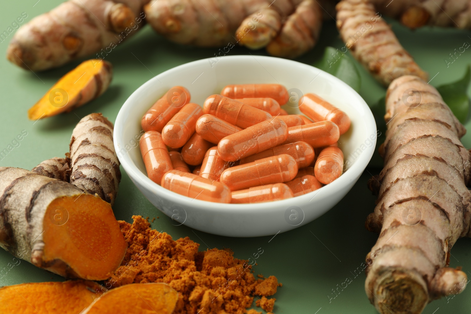 Photo of Aromatic turmeric powder, pills and raw roots on green background, closeup