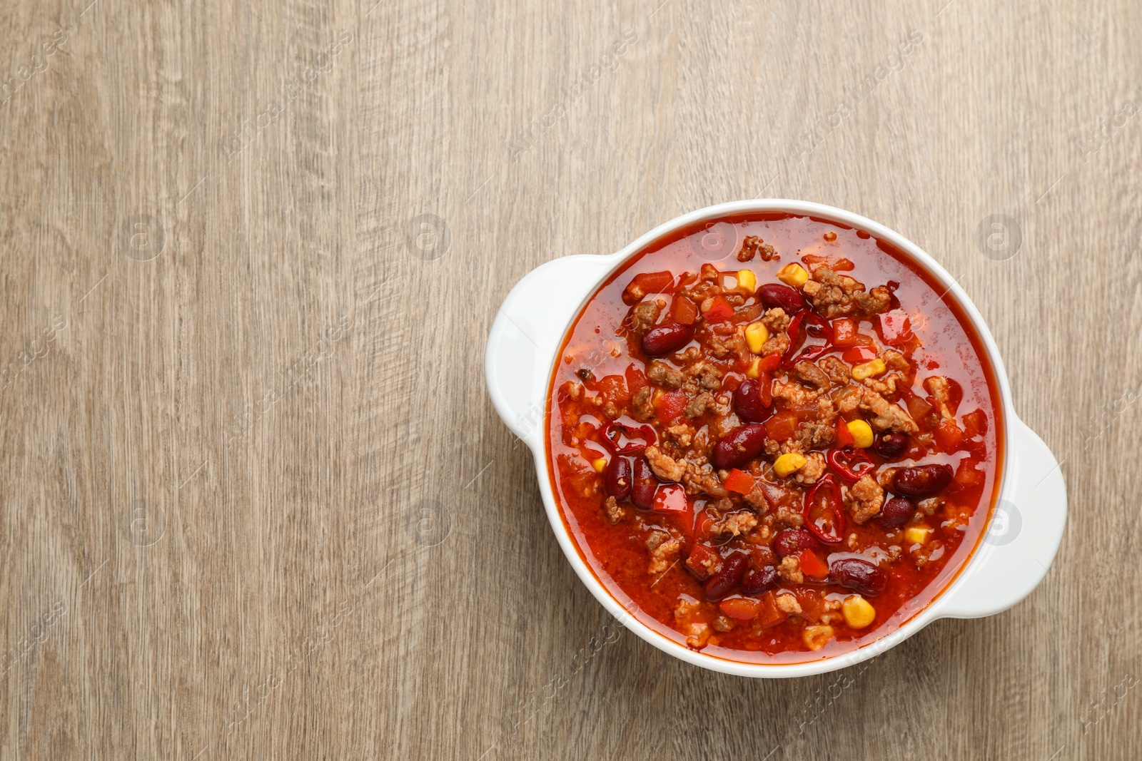 Photo of Bowl with tasty chili con carne on wooden table, top view. Space for text