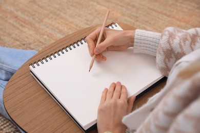 Photo of Woman drawing in sketchbook with pencil on floor at home, closeup