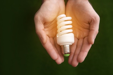 Photo of Man holding energy saving bulb for lamp on green background, top view