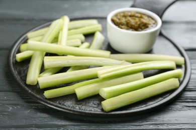 Photo of Slate board with celery sticks and dip sauce on grey wooden table, closeup