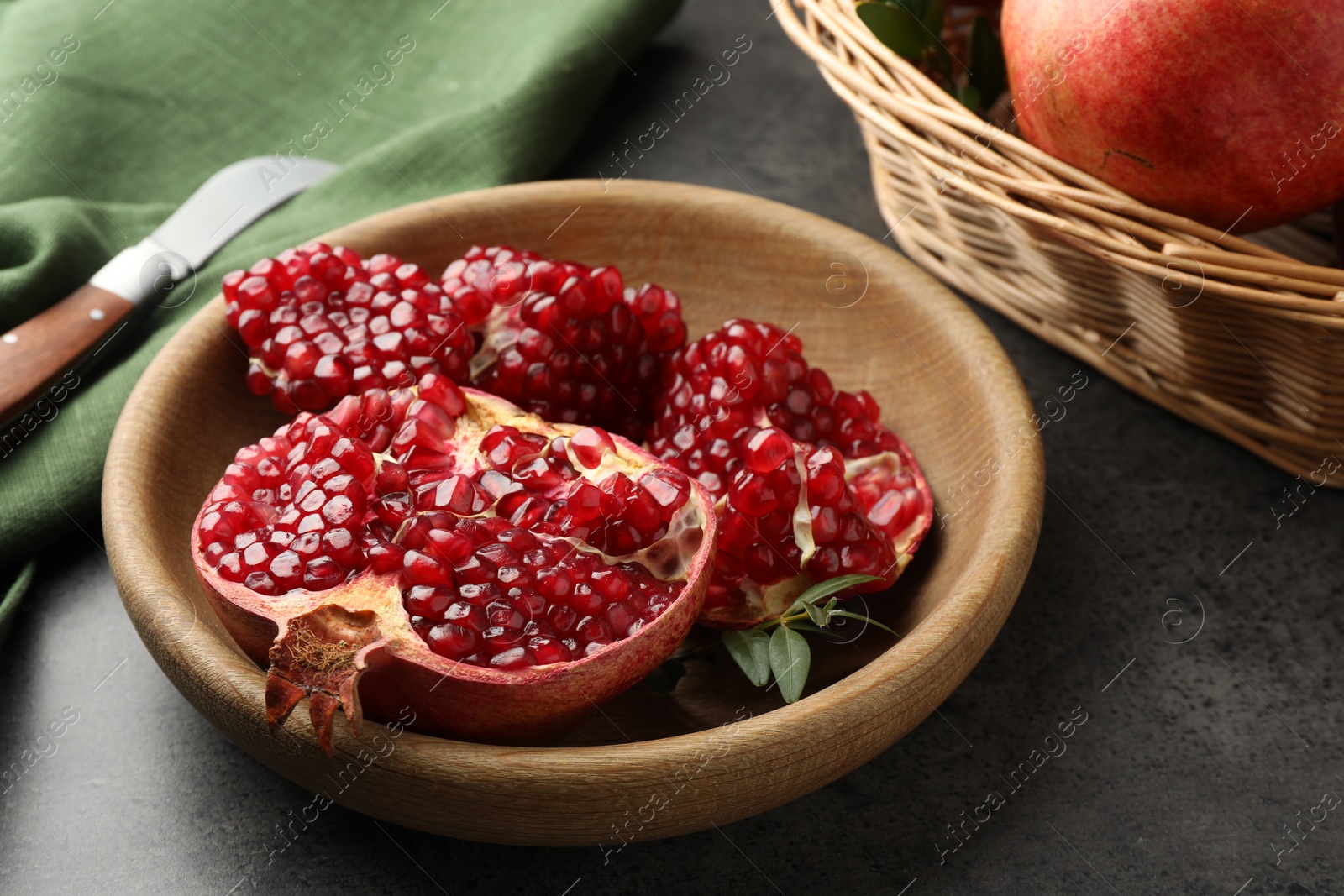 Photo of Cut fresh pomegranate, green leaves and knife on grey table, closeup