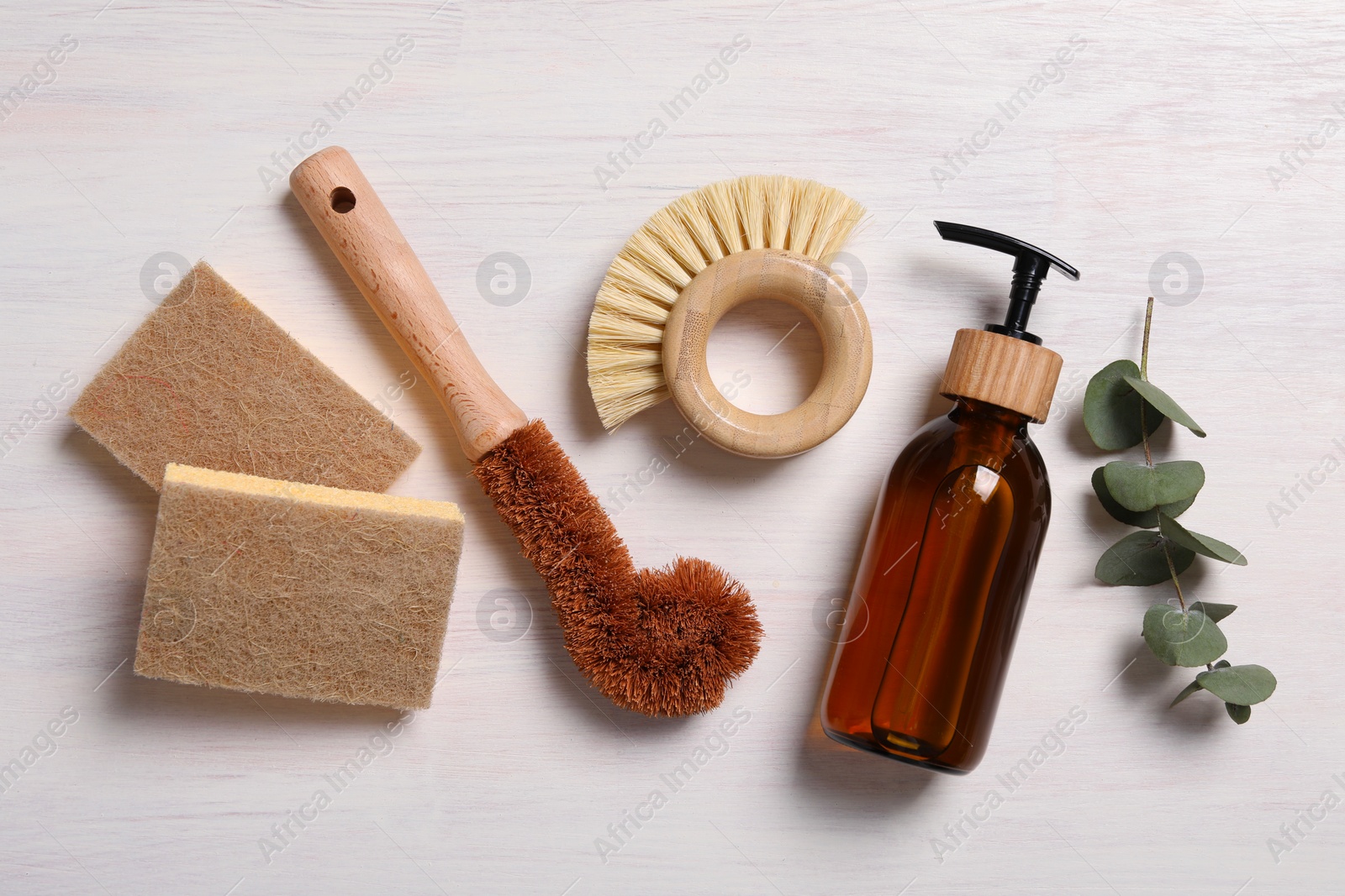 Photo of Cleaning brushes, sponges, dispenser and eucalyptus leaves on light wooden table, flat lay