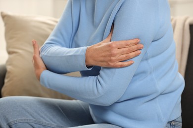 Photo of Mature woman suffering from pain in arm indoors, closeup. Rheumatism symptom