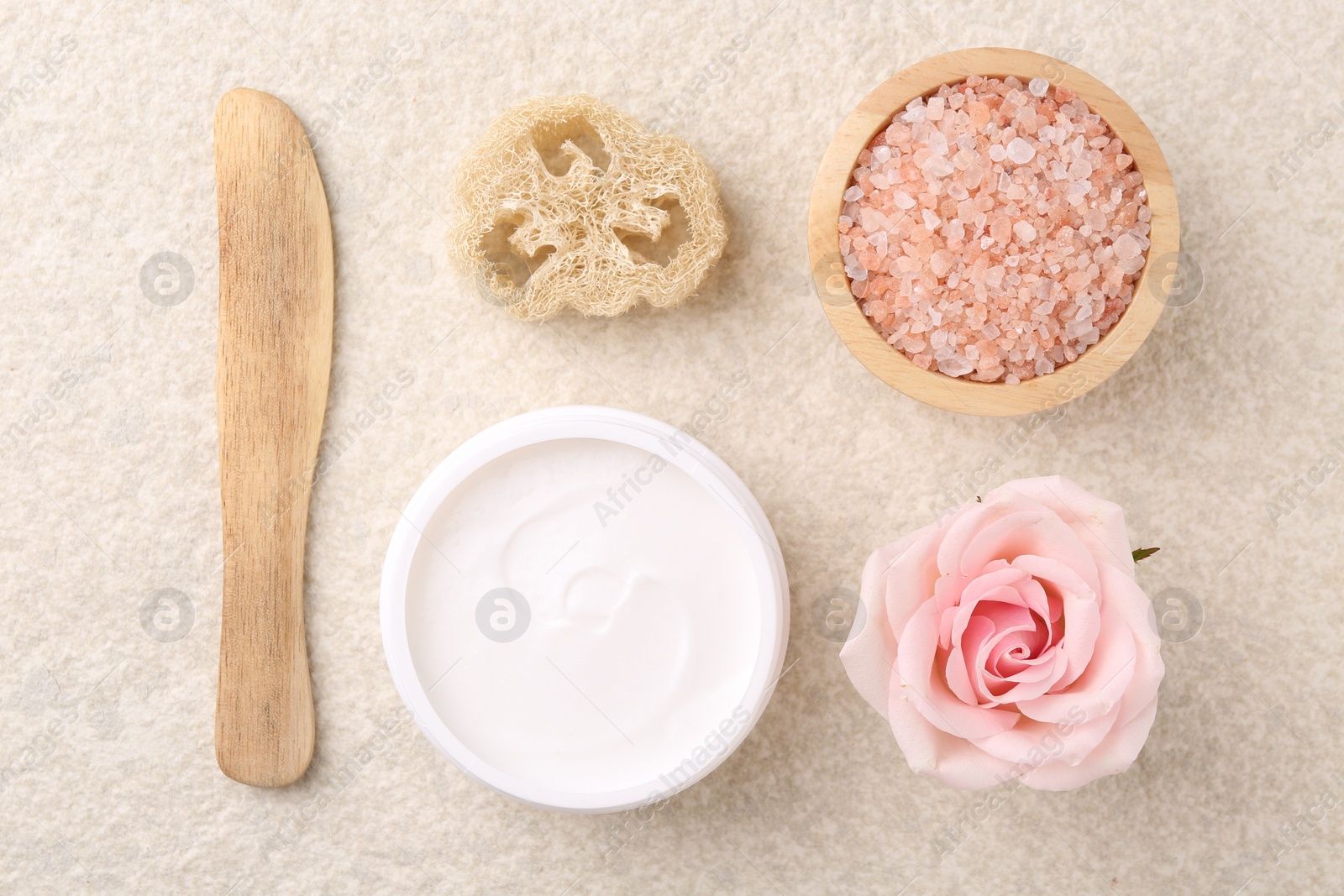 Photo of Flat lay composition with moisturizing cream in open jar and other body care products on light textured table