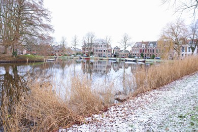 Photo of Picturesque view of water canal with moored boats, trees and buildings in city on winter day