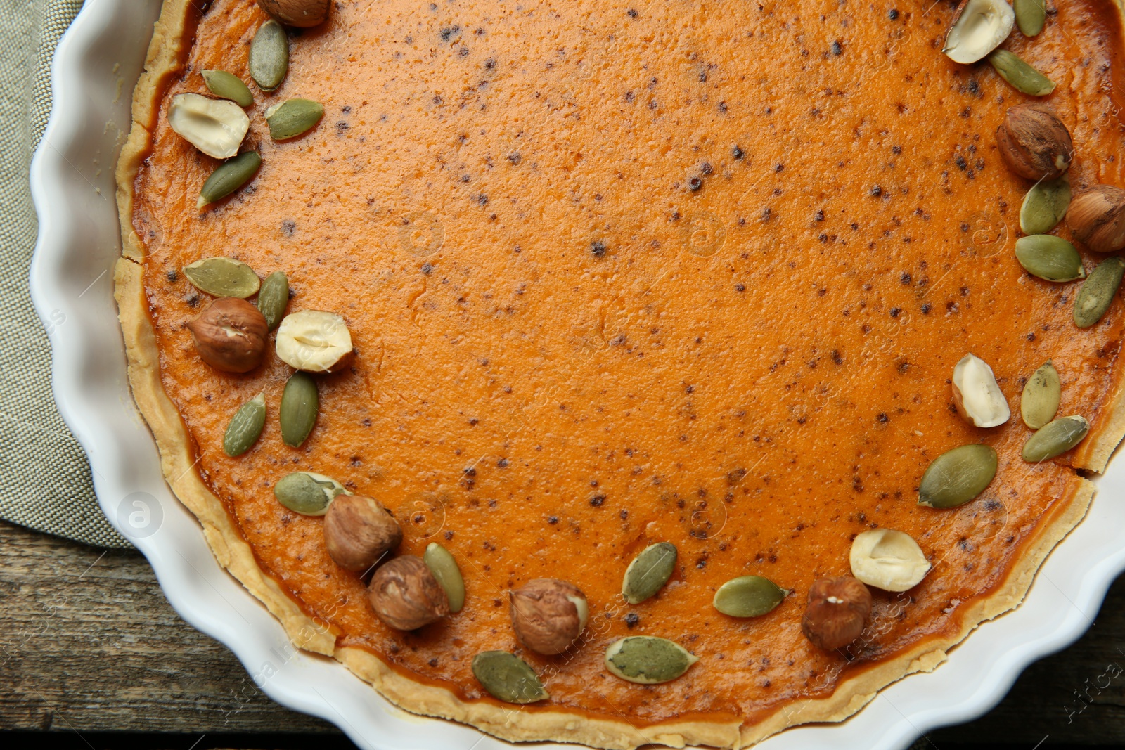 Photo of Delicious pumpkin pie with seeds and hazelnuts on wooden table, top view