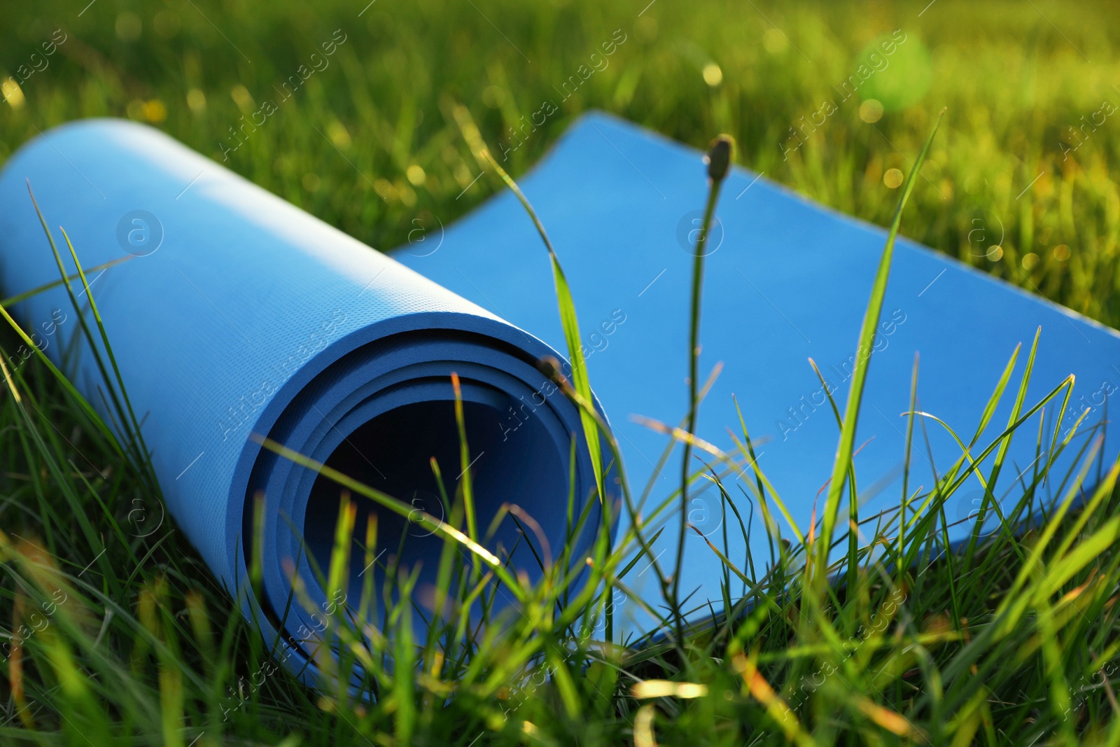 Photo of Blue karemat or fitness mat in fresh green grass outdoors, closeup