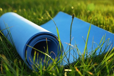 Photo of Blue karemat or fitness mat in fresh green grass outdoors, closeup