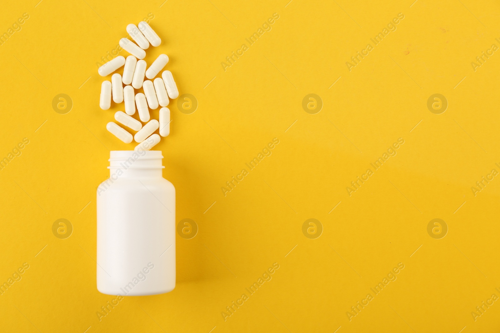 Photo of Bottle and vitamin capsules on yellow background, top view. Space for text