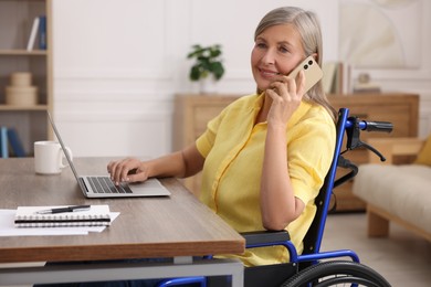 Woman in wheelchair talking on smartphone at table in home office