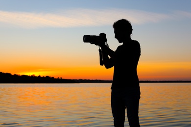 Photo of Young male photographer taking photo of riverside sunset with professional camera outdoors