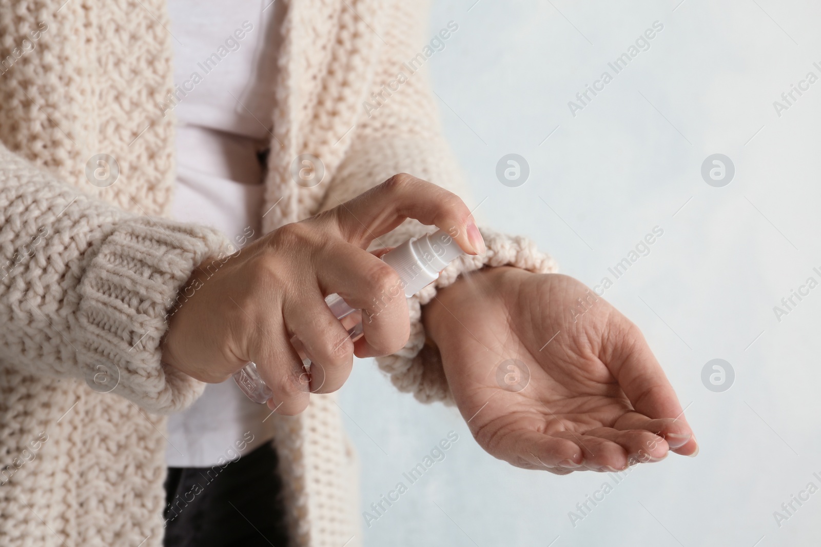 Photo of Woman spraying antiseptic onto hand against light background, closeup. Virus prevention