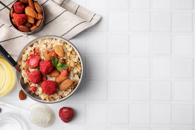 Photo of Delicious oatmeal with freeze dried strawberries, almonds and mint served on white tiled table, flat lay. Space for text