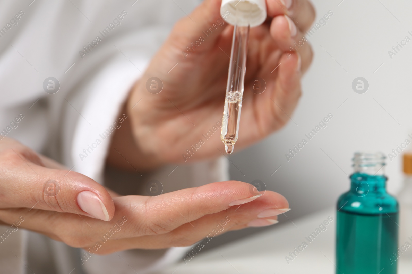 Photo of Woman applying cosmetic serum onto her finger at white table, closeup