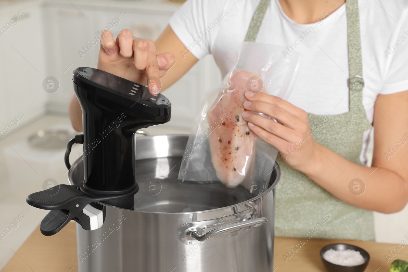 Photo of Woman putting vacuum packed meat into pot and using thermal immersion circulator, closeup. Sous vide cooking