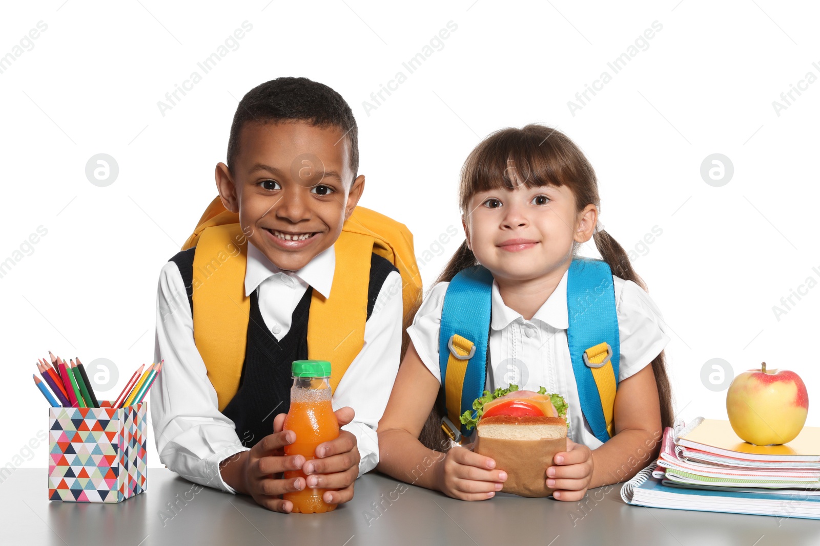 Photo of Schoolchildren with healthy food and backpacks sitting at table on white background