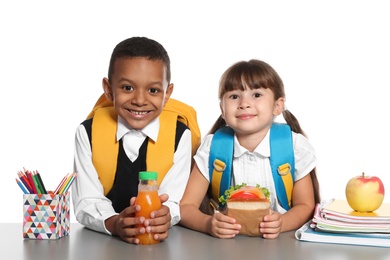 Photo of Schoolchildren with healthy food and backpacks sitting at table on white background