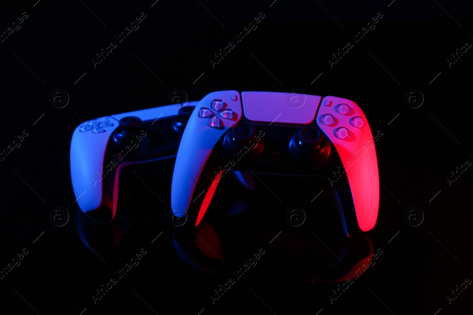 Photo of Wireless game controllers on black mirror surface in neon lights