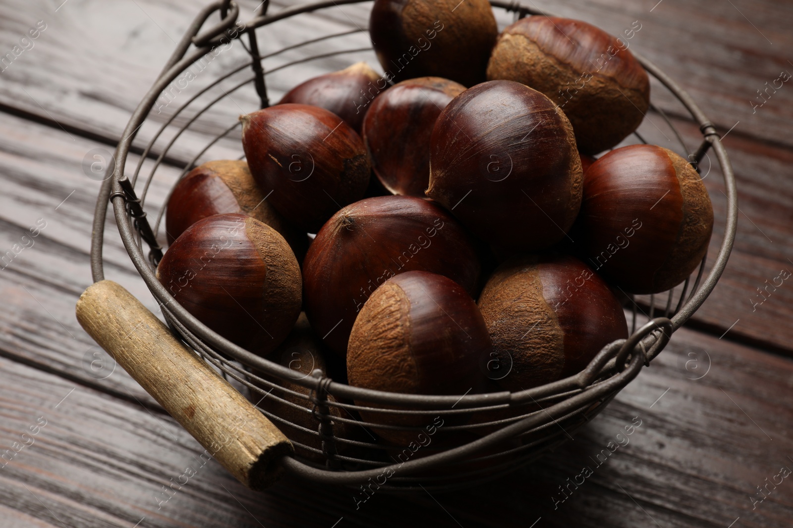 Photo of Sweet fresh edible chestnuts in metal basket on wooden table, closeup