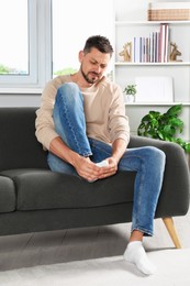 Photo of Man suffering from foot pain on sofa at home