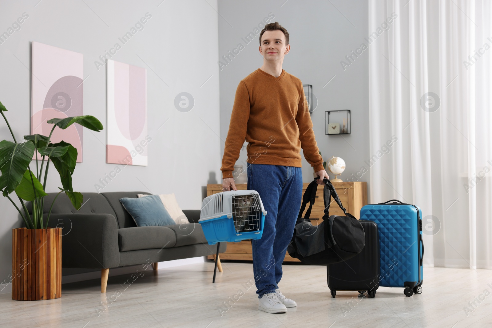 Photo of Travel with pet. Man holding carrier with cute cat and bag at home