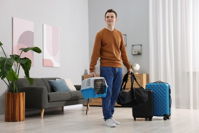 Photo of Travel with pet. Man holding carrier with cute cat and bag at home