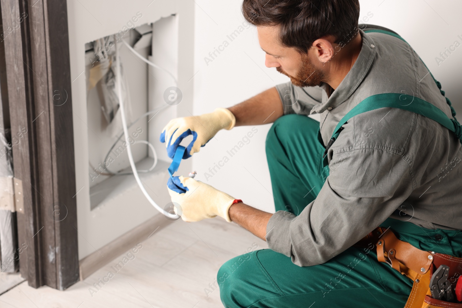 Photo of Electrician fixing wires with insulating tape indoors